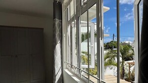A room with a large window, a wardrobe, and a view of a balcony with plants.