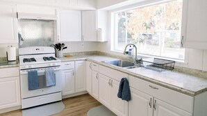 Una cucina con mobili bianchi, un fornello, un lavello e una finestra con vista sugli alberi.