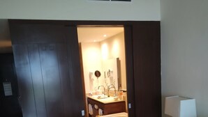 Ein Hotelzimmer mit Bett, Nachttisch mit Lampe, Badezimmer mit Waschbecken, Spiegel und Badewanne.