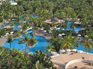 Un resort con varias piscinas rodeado de palmeras y sillas de descanso.