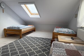 A small attic bedroom with two wooden beds, a skylight, a clock, and a patterned rug. - Comfortable Holiday Home With a Private Garden (Ustka)