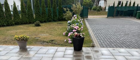 A paved driveway leading to a house with a garden in the foreground.
