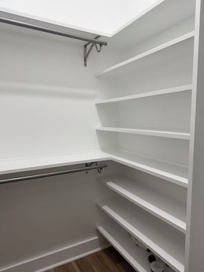 A white closet with multiple shelves and a metal rod for hanging items. - Modern 3BR Family Home - Large Backyard, Kid-Friendly, Minutes from Downtown! (New Orleans)