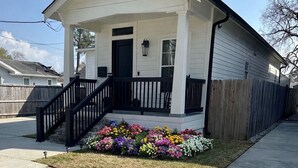 A residential house with a front porch, a wooden fence, and a flower bed. - Modern 3BR Family Home - Large Backyard, Kid-Friendly, Minutes from Downtown! (New Orleans)
