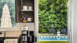 A kitchen with a coffee bar, a coffee maker, a filter box, and a cabinet with mugs and a box of coffee. - Casa Tulum Sol | Boho Pool Retreat Near Beach (Dania Beach)