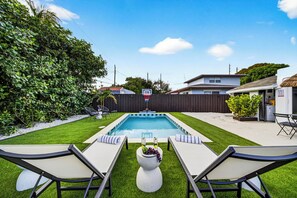 En baghave med swimmingpool, to liggestole og et lille haveareal med en dekorativ vase.