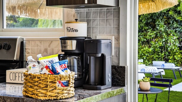 A kitchen with a coffee maker, a basket of snacks, and a coffee sign. - Casa Tulum Sol | Boho Pool Retreat Near Beach (Dania Beach)