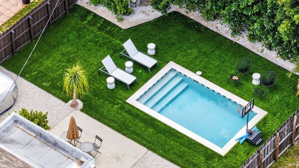En baghave med en swimmingpool, en terrasse med stole og et bord, og et lille haveområde.