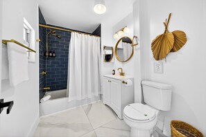 Et moderne badeværelse med et hvidt toilet, et badekar med hvid gardin, en hvid vask med guldfarvede armaturer og et bruseområde med blå fliser.