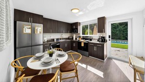 A modern kitchen with dark wood cabinets, stainless steel appliances, and a dining area with wicker chairs and a white table set for four. - Casa Tulum Sol | Boho Pool Retreat Near Beach (Dania Beach)