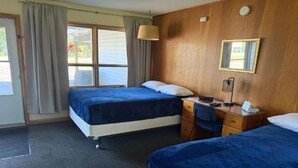 Habitación de hotel con dos camas, un escritorio, una silla, una lámpara y una ventana con cortinas.