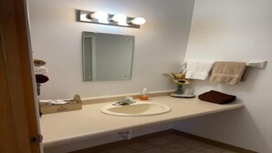 Un baño con lavamanos, espejo, toallero y un cesto de basura.