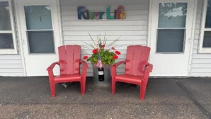 Un porche con dos sillones Adirondack rojos, una maceta con flores rojas y un letrero que dice 'River Life'.