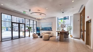 Un hall d’entrée spacieux au design moderne, comprenant un coin salon avec des canapés et une table basse, de grandes fenêtres donnant sur la rue et une grande peinture abstraite au mur.
