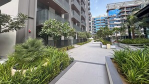 Un immeuble résidentiel moderne situé en milieu urbain, doté de balcons, d’un chemin central et entouré de verdure.