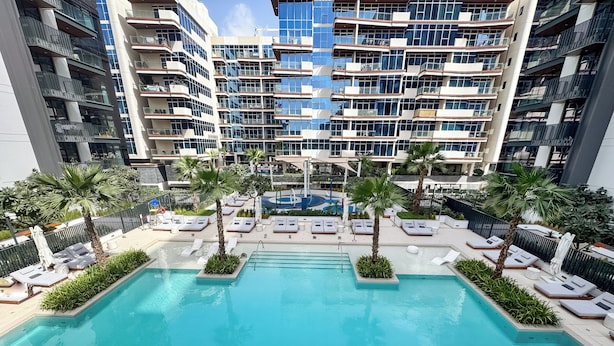 Un hôtel moderne doté d’une piscine centrale, entourée d’espaces de détente et de palmiers.