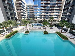 Ein modernes Hotel mit einem zentral gelegenen Schwimmbad, umgeben von Liegebereichen und Palmen.