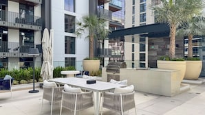 Un espace extérieur aménagé en patio, avec une table à manger, des chaises, un barbecue et des plantes en pot.