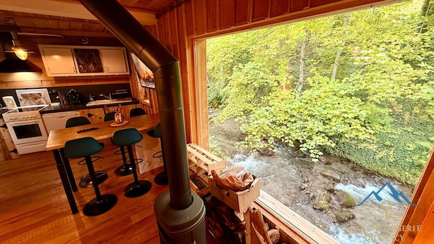 Ein rustikales Blockhaus-Interieur mit Küche, Barbereich und einem Fenster mit Blick auf einen bewaldeten Bach.