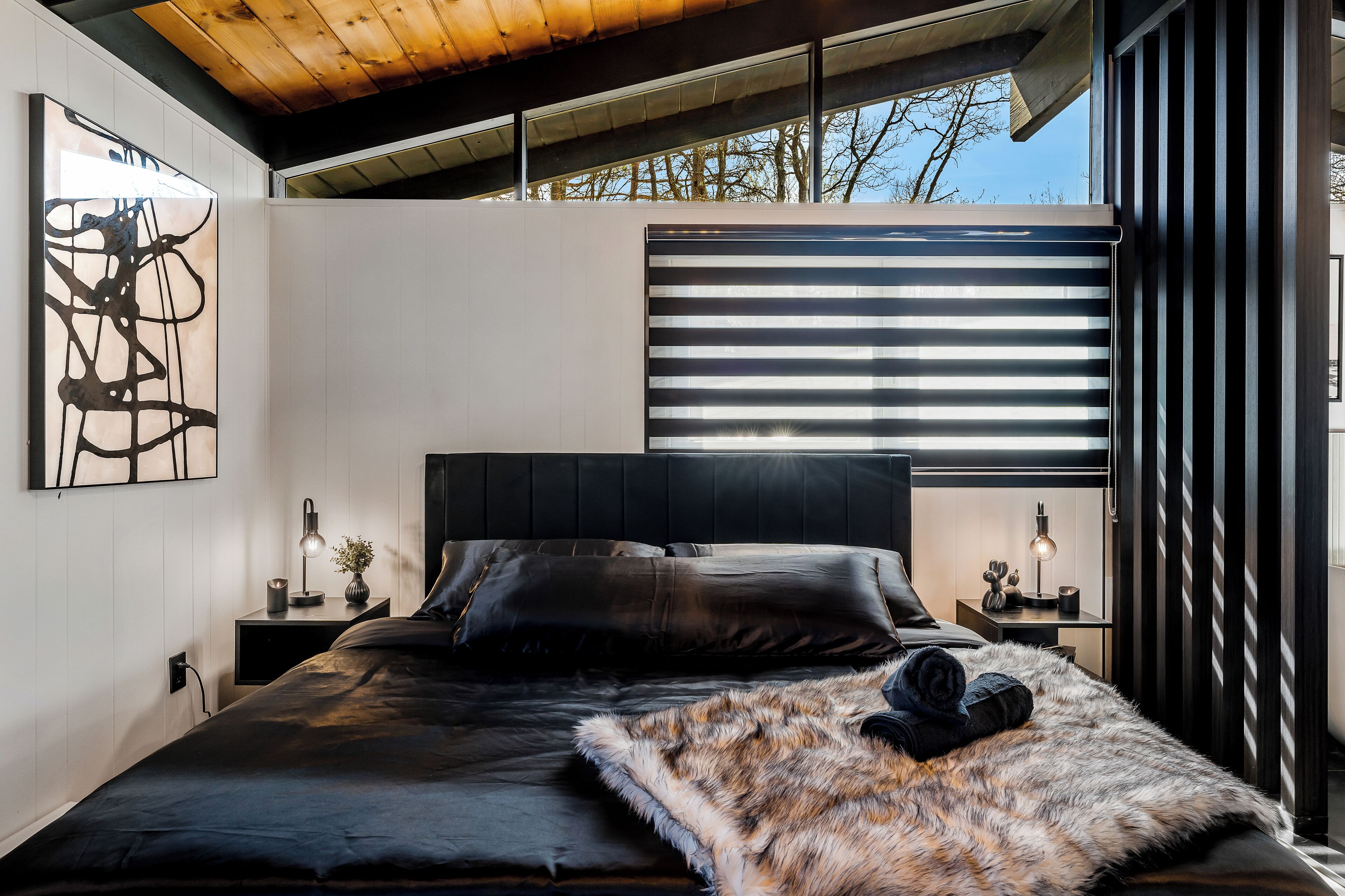 Een moderne slaapkamer met een groot bed, een hoofdbord, nachtkastjes en een raam met jaloezieën.