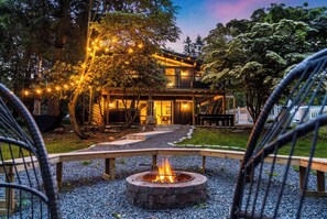 Ein modernes Haus mit Feuerstelle im Garten, umgeben von Bäumen und Kies.