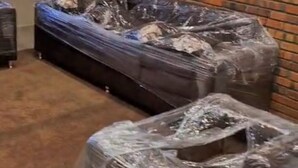 Et værelse med en murstensvæg, en sofa betrukket med plastik og et tæppedækket gulv.