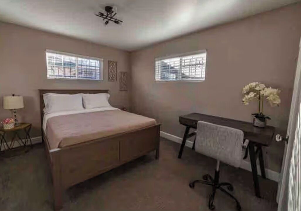 Een slaapkamer met een bed, een bureau, een stoel, een lamp en een raam.