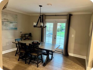 Un comedor con una mesa y sillas de madera, una lámpara colgante y vistas al exterior a través de puertas de vidrio.