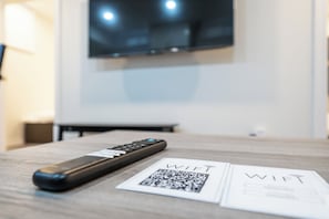 Un control remoto y un código QR para WiFi sobre una mesa de madera en una habitación con un televisor montado en la pared.