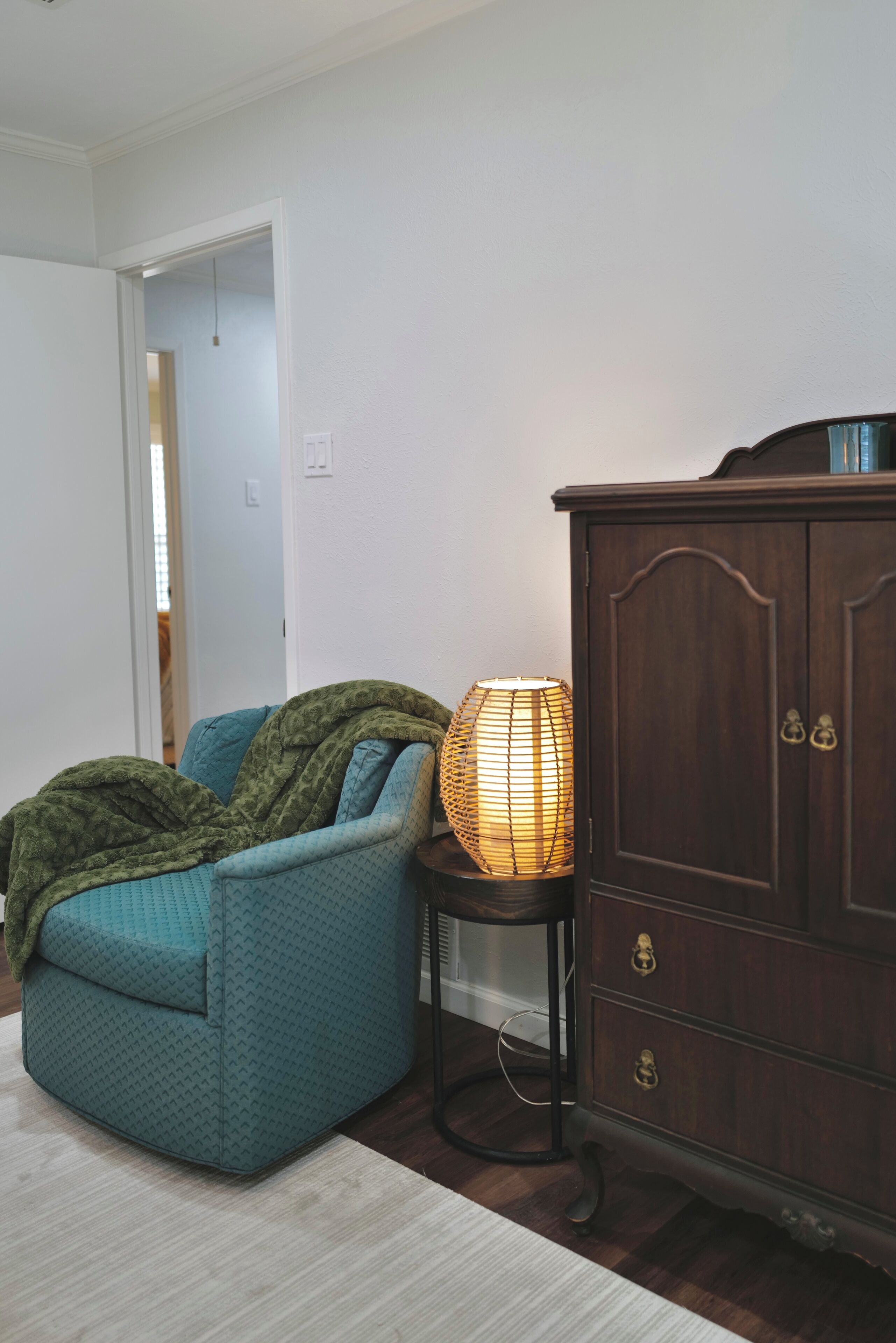 A room with a teal armchair, a wooden cabinet, and a floor lamp.