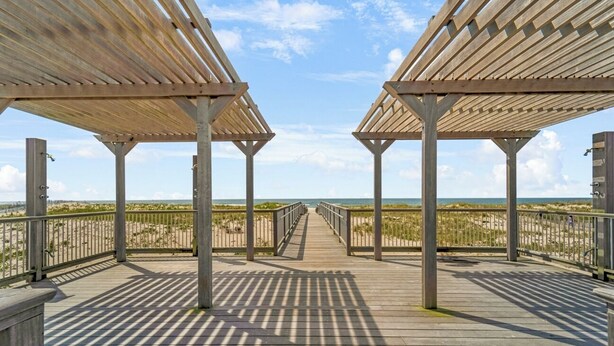 Een houten vlonder die naar het strand leidt, onder een heldere lucht.