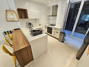 Une cuisine moderne avec des meubles blancs, un four encastré, une cuisinière à gaz et un petit îlot central doté d’un évier.
