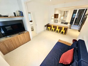 Un salon moderne doté d’un téléviseur à écran plat, d’un meuble de rangement en bois et d’un canapé bleu foncé agrémenté d’un coussin rouge.