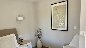 A neatly arranged bedroom with a bed, a chair, a nightstand, a vase with flowers, and a framed artwork on the wall. - 2-br Countryside Apartment in Mouzaki (Zakynthos)