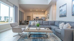 Un salon moderne avec un canapé gris, une table basse et, au fond, un coin repas.