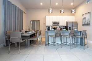 A modern kitchen with stainless steel appliances, a dining area with a large table and chairs, and pendant lighting. - Premium Location Spectrum at Reunion Near Disney (Kissimmee)