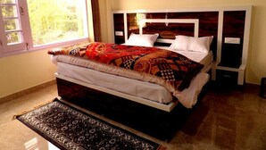 Quarto com uma cama grande, janela com cortinas e mesa de cabeceira com televisão.