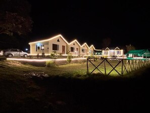 Un conjunto de cabañas iluminadas durante la noche, con un coche estacionado en la entrada.