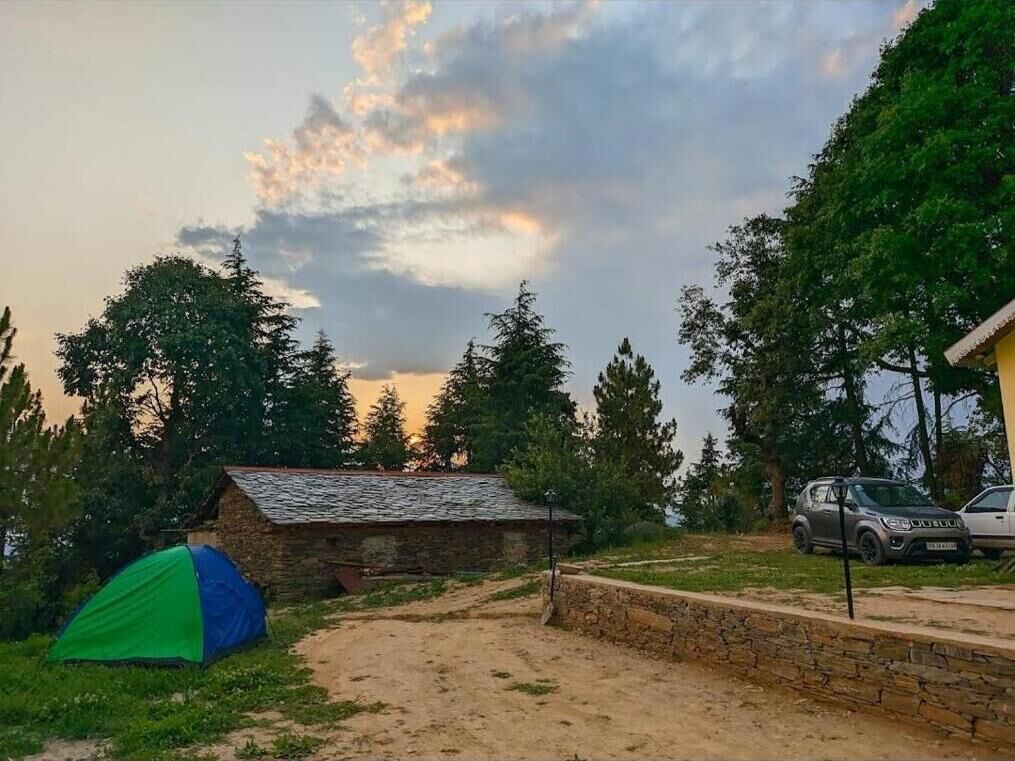 A rustic cabin with a dirt path leading to it, surrounded by trees and a tent.