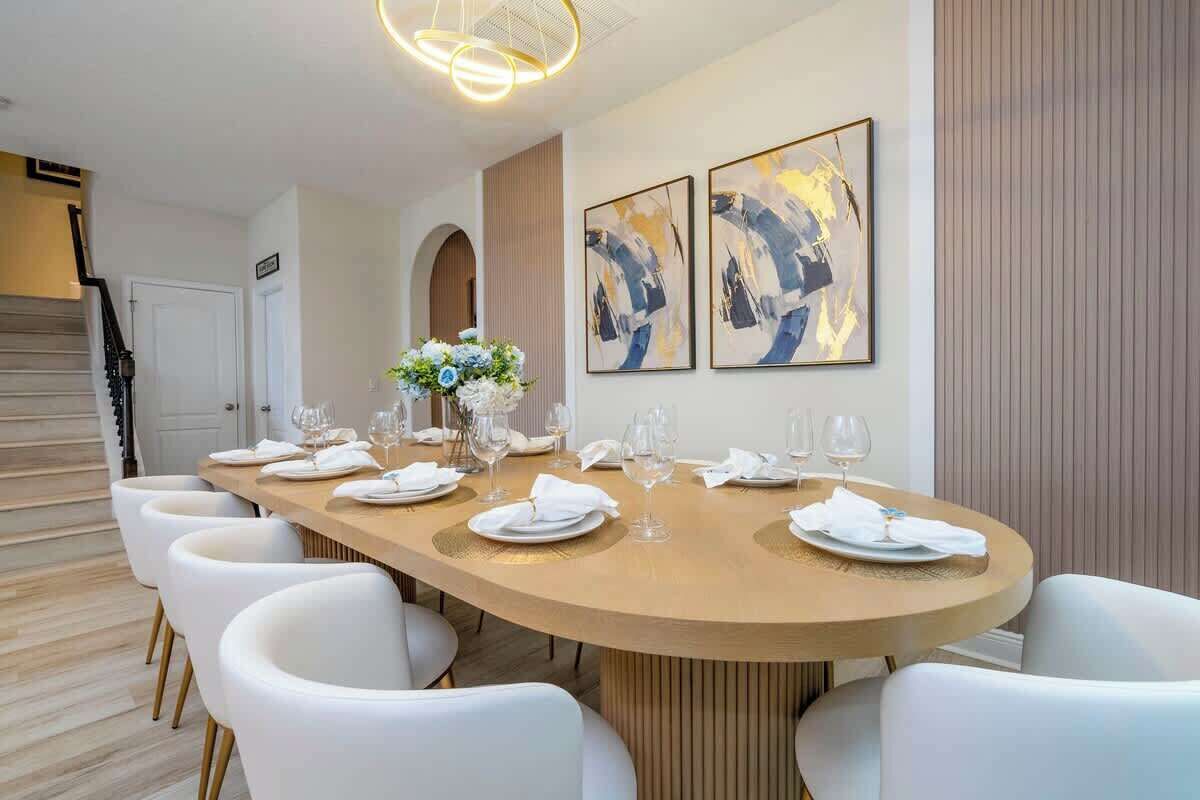 A modern dining room with a long table set for six, white chairs, and abstract art on the walls.