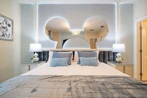 Ein modernes Hotelzimmer mit einem großen Bett, zwei Nachttischen mit Lampen, einem großen Spiegel und einem Wandbild mit Mickey Mouse.