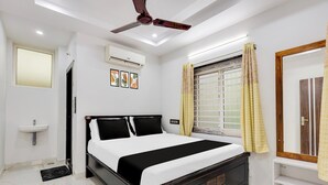 A bedroom with a bed, a ceiling fan, a window with curtains, a bedside table, and a wall-mounted air conditioner. - Hotel O Kotipalli (Rajahmundry)