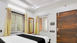 A hotel room with a bed, two windows with curtains, a wooden door, and a ceiling light. - Hotel O Kotipalli (Rajahmundry)