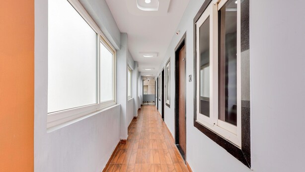 A long, narrow hallway with large windows on one side and doors on the other. - Hotel O Kotipalli (Rajahmundry)