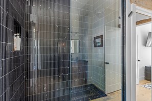 A modern bathroom with black tiled walls, a glass shower enclosure, and a visible showerhead. - The Night Owl at Lake Martin - 3BR/3BA Home in Eclectic (Eclectic)