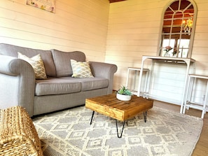 A cozy living room with a grey sofa, patterned cushions, a wooden coffee table with a plant, and a patterned rug. - Cosy cabin, w/modern comforts minutes away from popular beaches & seaside towns. (Old Romney)