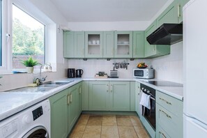Een keuken met groene kastjes, een wasmachine, een magnetron en een waterkoker.