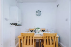 Un comedor con una mesa y sillas de madera, un reloj en la pared y un radiador blanco.