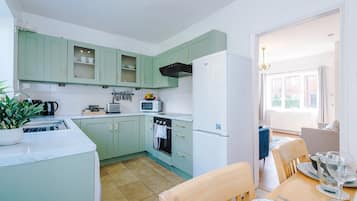 A compact kitchen with green cabinets, a white refrigerator, and a dining area with a table and chairs.