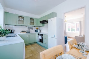 A compact kitchen with green cabinets, a white refrigerator, and a dining area with a table and chairs.